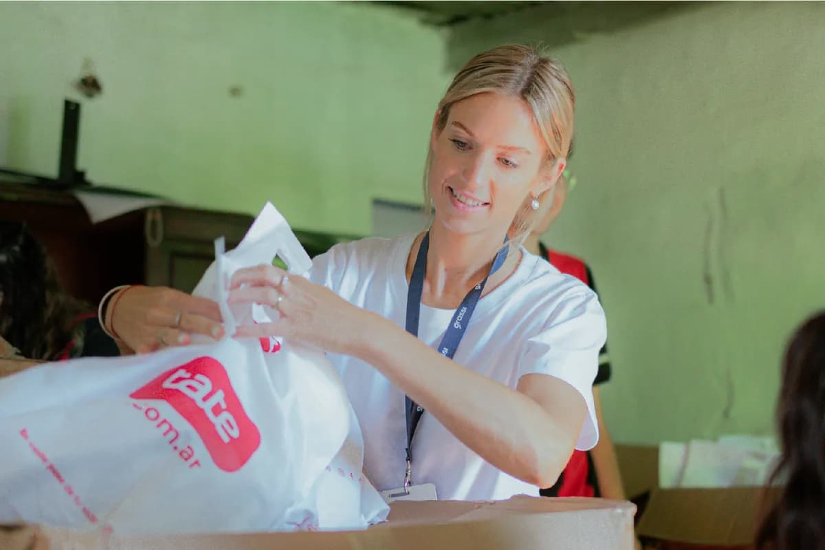 Una voluntaria entrega una bolsa con útiles escolares a un nene en un merendero