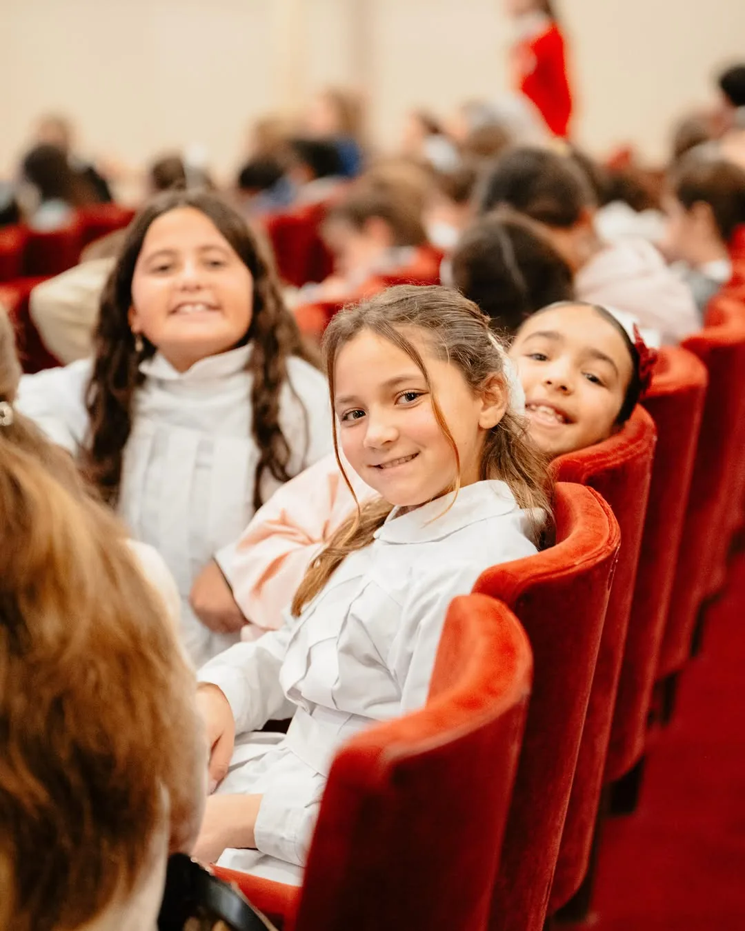 Tres nenas sonríen sentadas en las butacas de un teatro durante una jornada de la fundación